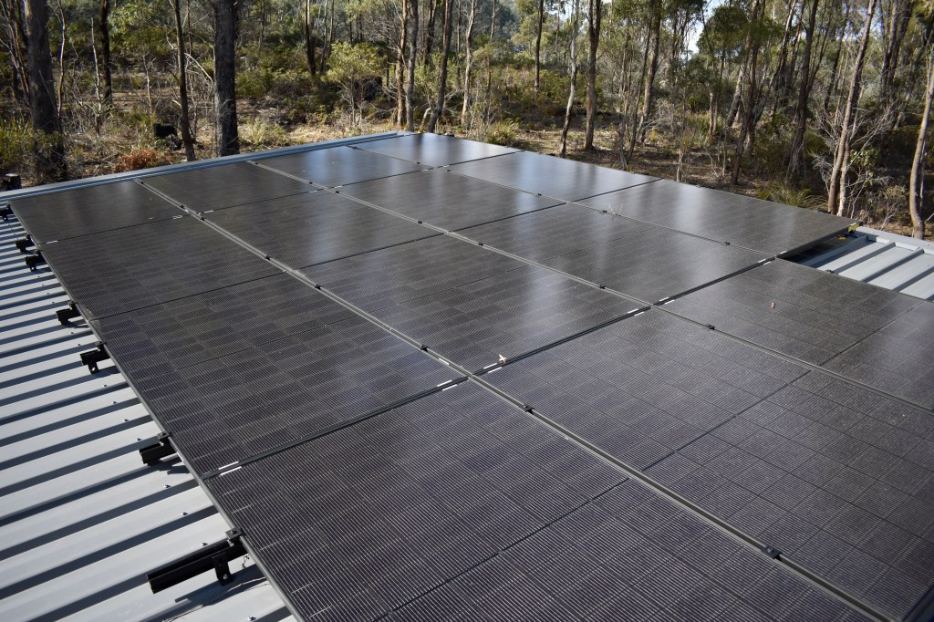 An image depicting several solar panels mounted on a rooftop in the bush.