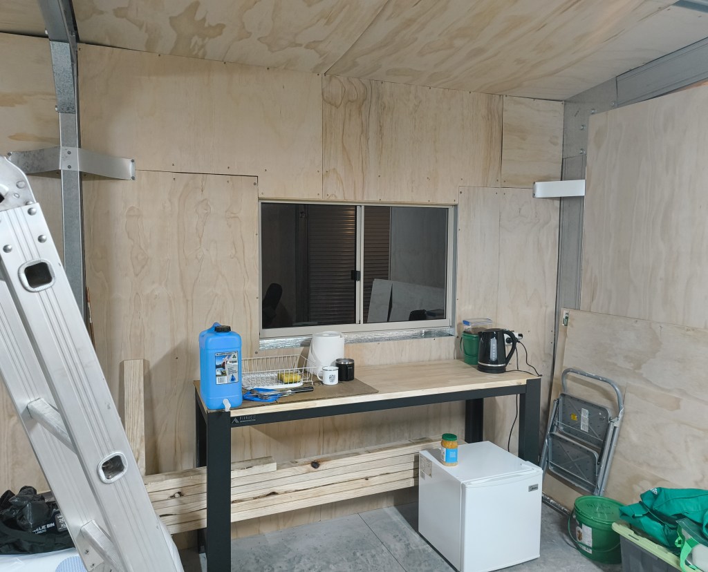 An image of a workbench with a kettle and bar fridge, indicating that it is being used as a makeshift kitchen.