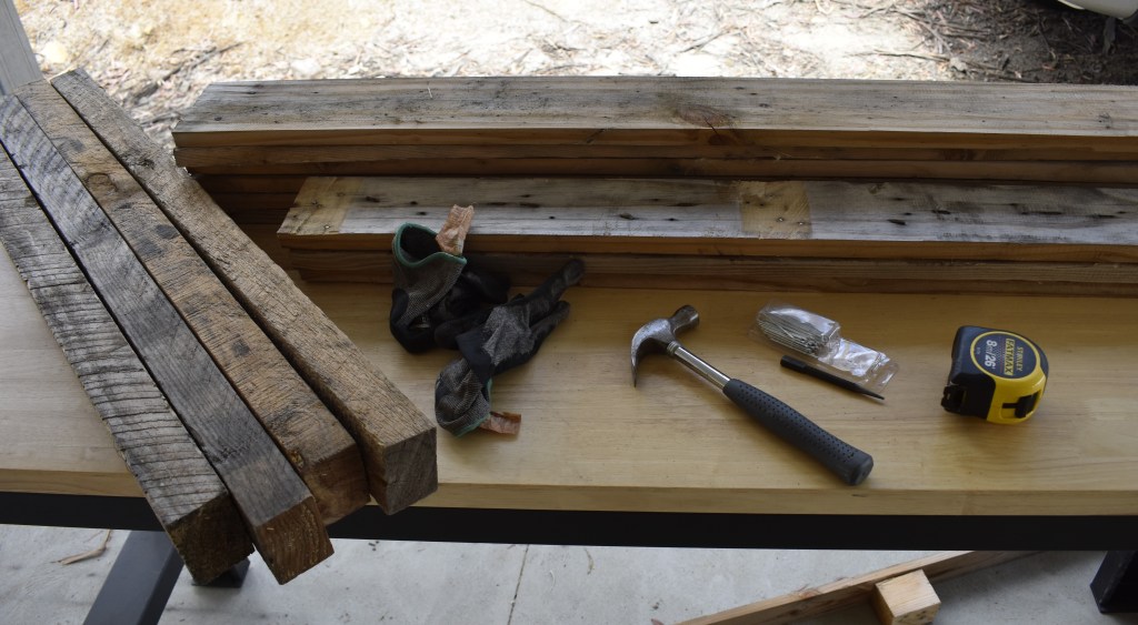A selection of timber shipping pallet parts laid out onto a work bench with a few tools scattered about.